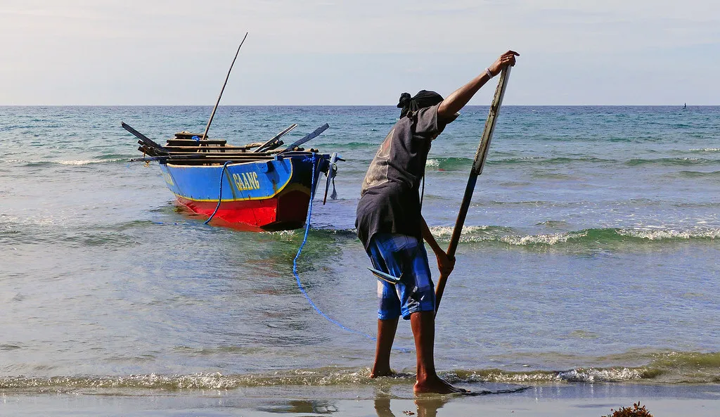 A man pushing a painted wooden fishing boat off a tropical beach
